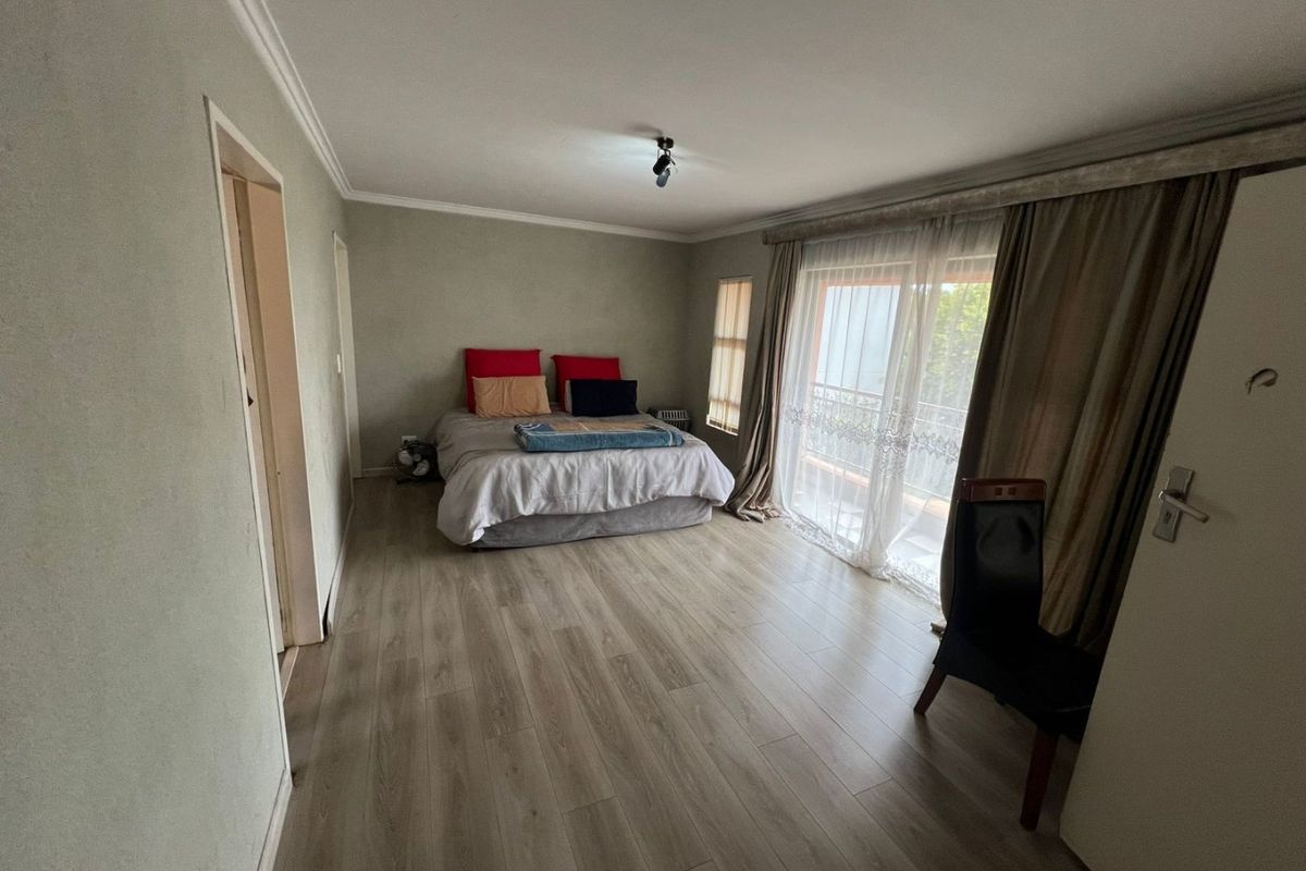 Spacious bedroom featuring light-toned laminate flooring, cove cornicing, and a sliding glass door providing direct access to an outdoor balcony.
