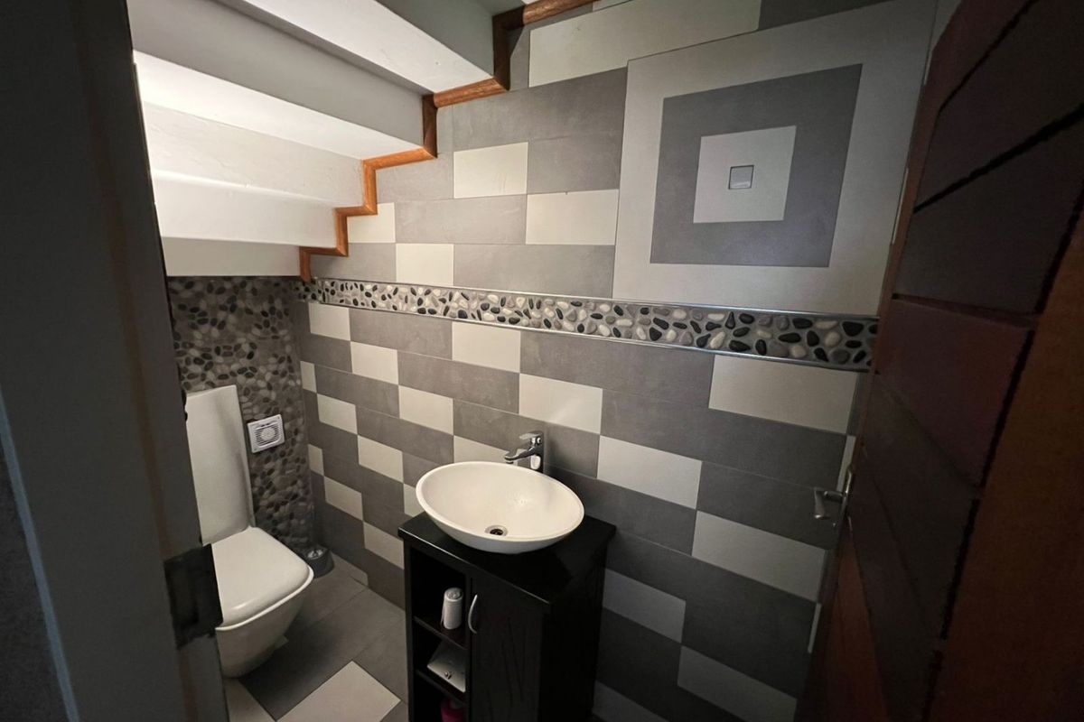 Compact guest bathroom featuring a vessel sink, vanity cabinet, and modern tiled walls, situated conveniently under the staircase.