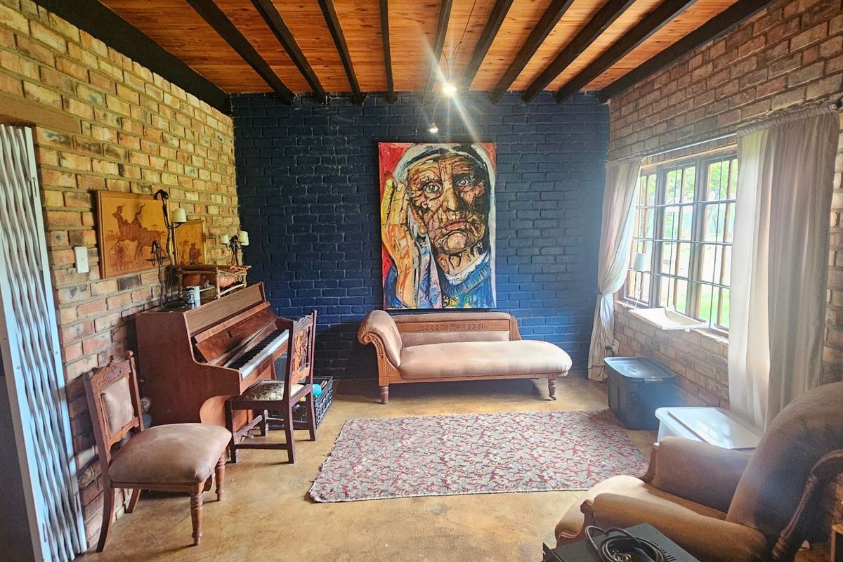 A rustic living room featuring exposed brick walls, a timber beam ceiling, and concrete flooring, offering a characterful and textured interior space.