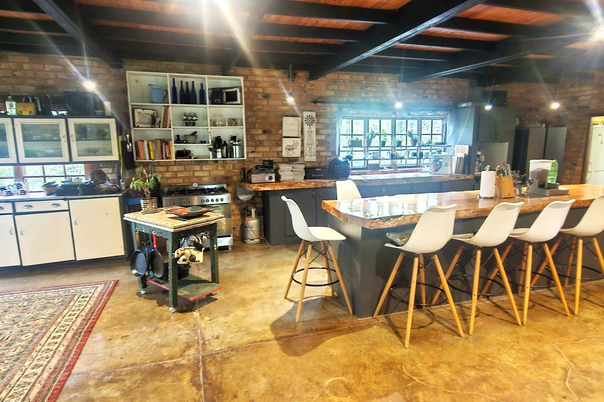 Spacious rustic kitchen featuring exposed brick walls, timber beam ceilings, polished concrete floors, and a large central island with a natural wood countertop.