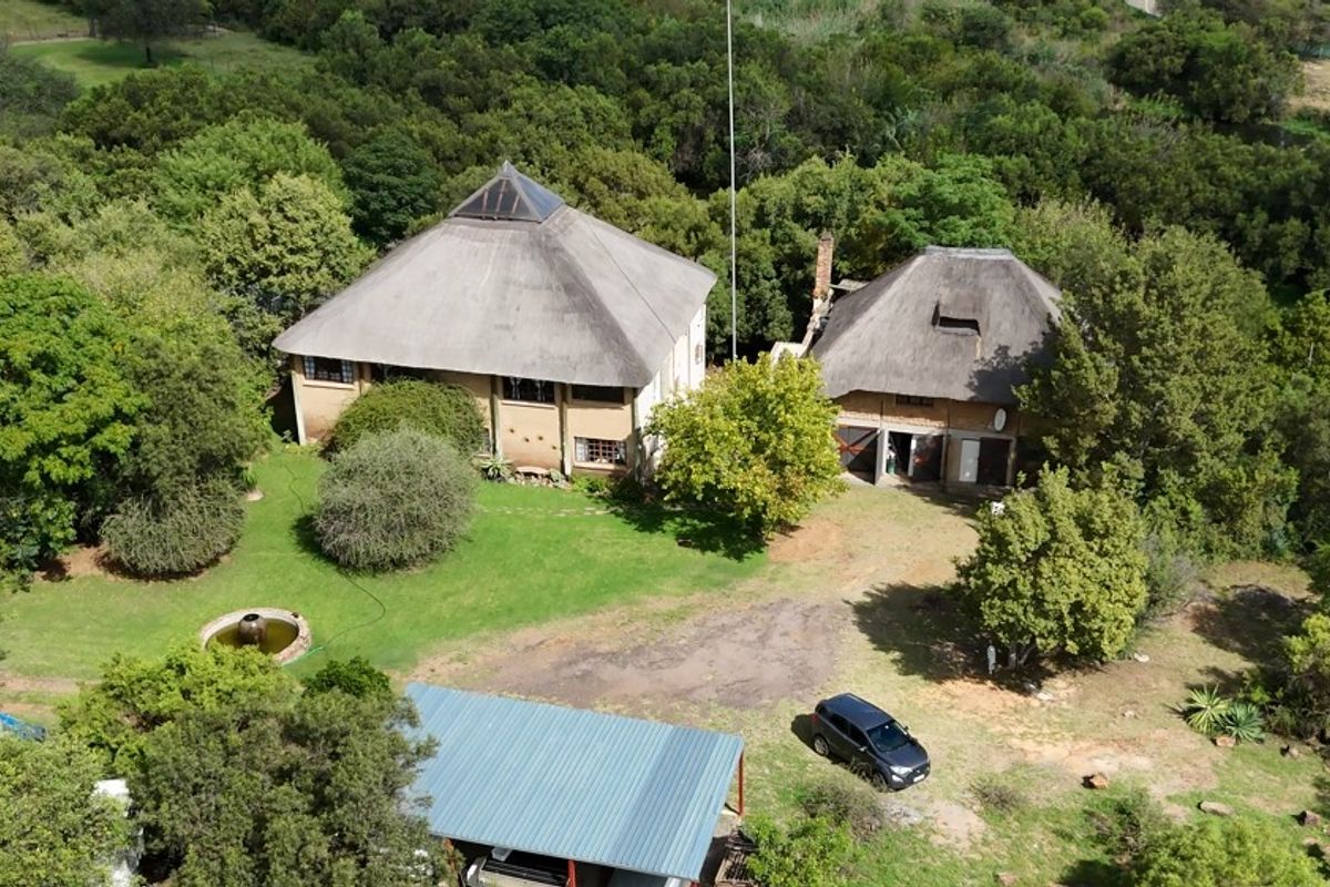 Aerial view of a farm property featuring two main structures with thatched roofs, a metal carport, and established garden surroundings.