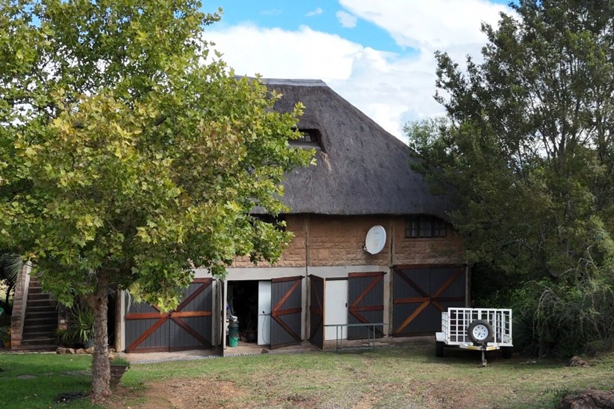 Rear view of a rustic farm building featuring traditional stone walls, a thatched roof, and multiple garage access points with an external staircase.