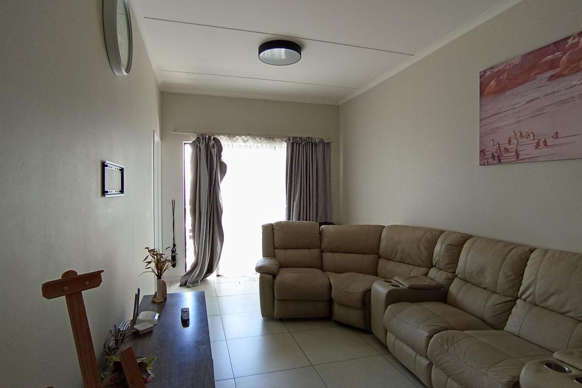 A functional living room featuring neutral tiled flooring and natural light access through a sliding door with curtain tracks.