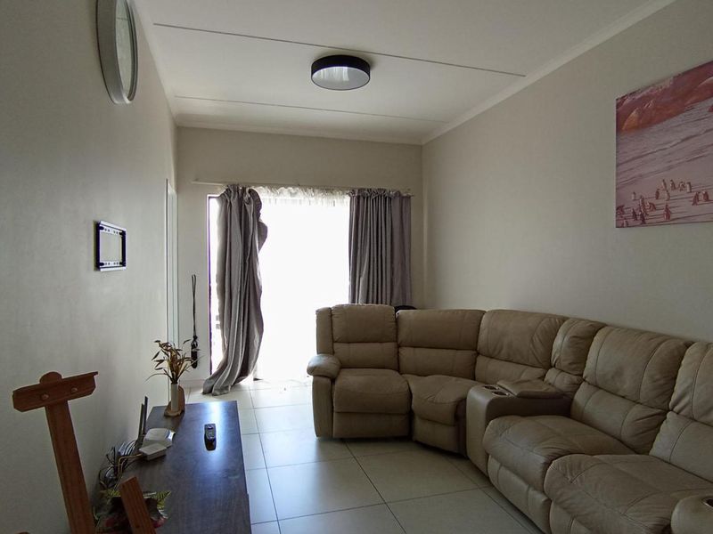 A functional living room featuring neutral tiled flooring and natural light access through a sliding door with curtain tracks.