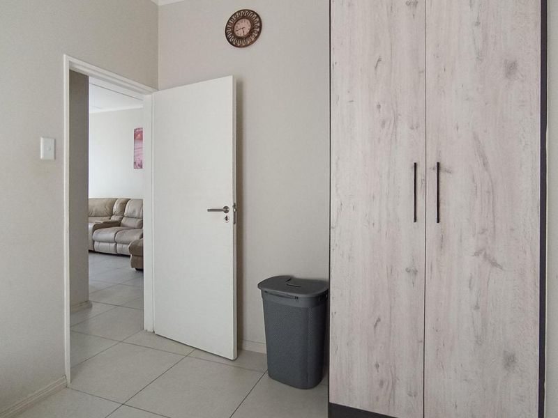 A bedroom featuring light-toned built-in wardrobes, neutral tiled flooring, and a doorway leading to an adjacent living area.