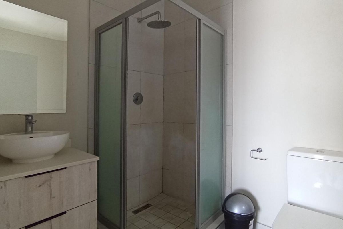 A clean, functional bathroom featuring a corner shower enclosure, a modern vanity with a vessel sink, and a standard toilet.