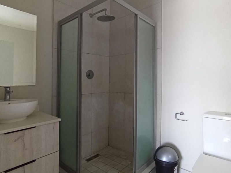 A clean, functional bathroom featuring a corner shower enclosure, a modern vanity with a vessel sink, and a standard toilet.
