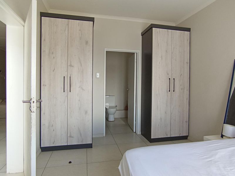 A bedroom featuring modern built-in cupboards with wood-grain finish, neutral tiled flooring, and direct access to an en-suite bathroom.
