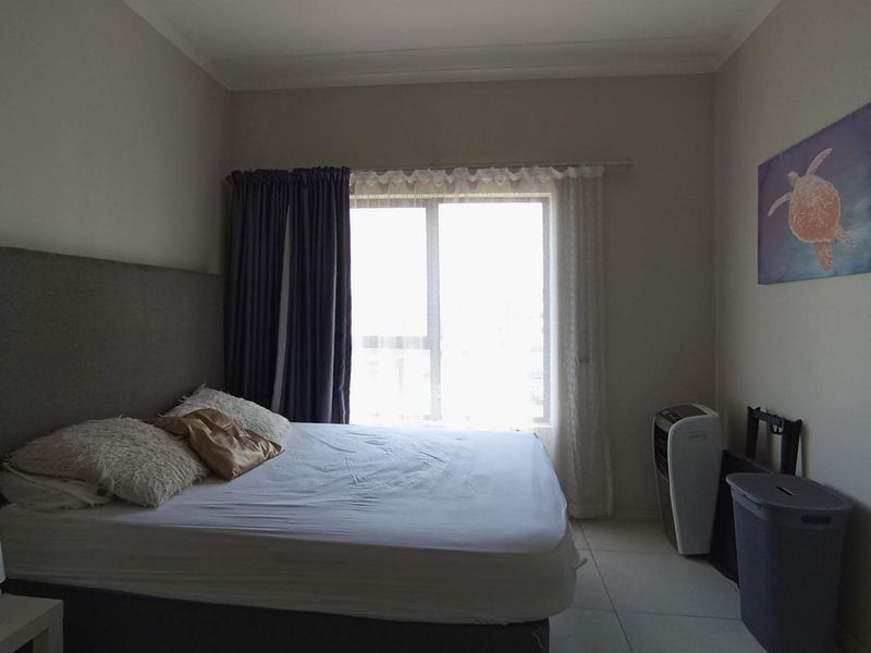 A bedroom featuring tiled flooring, a sliding window with curtains, and cove cornicing, providing a functional and neutral living space.