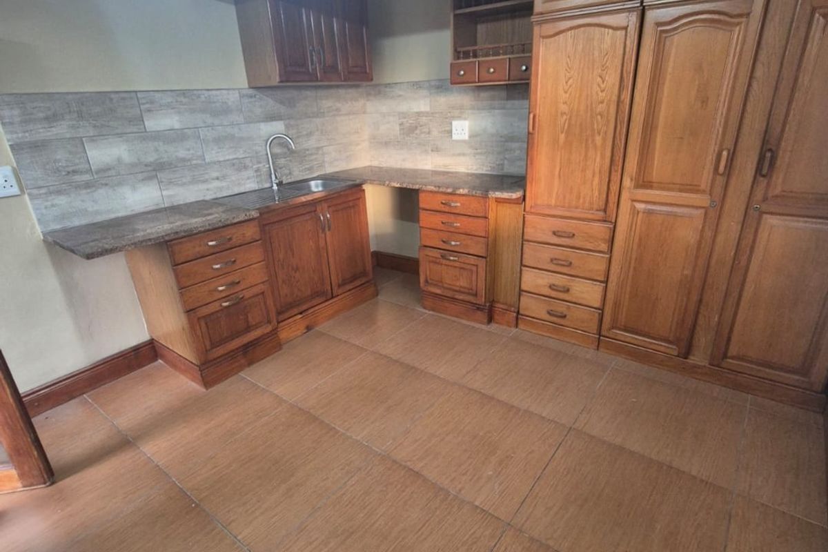 A functional scullery area featuring extensive wooden cabinetry, built-in pantry storage, a stainless steel sink, and durable tiled flooring.