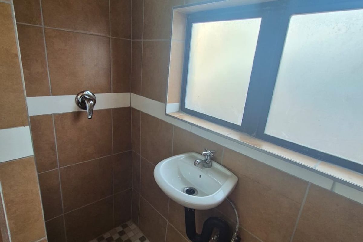 A compact bathroom featuring tiled walls and flooring, a wall-mounted basin, a shower area, and a toilet.