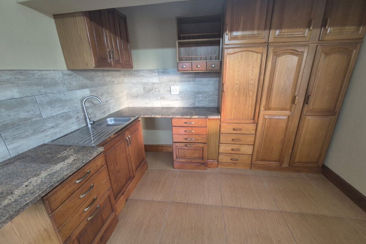 A functional kitchen area featuring wooden cabinetry, laminate countertops, a stainless steel sink, and tiled finishes throughout.