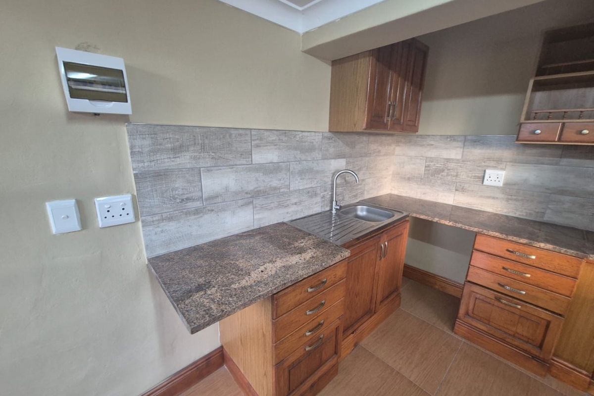 A functional kitchen area featuring wooden cabinetry, laminate countertops, a stainless steel sink, and modern tiled backsplash finishes.