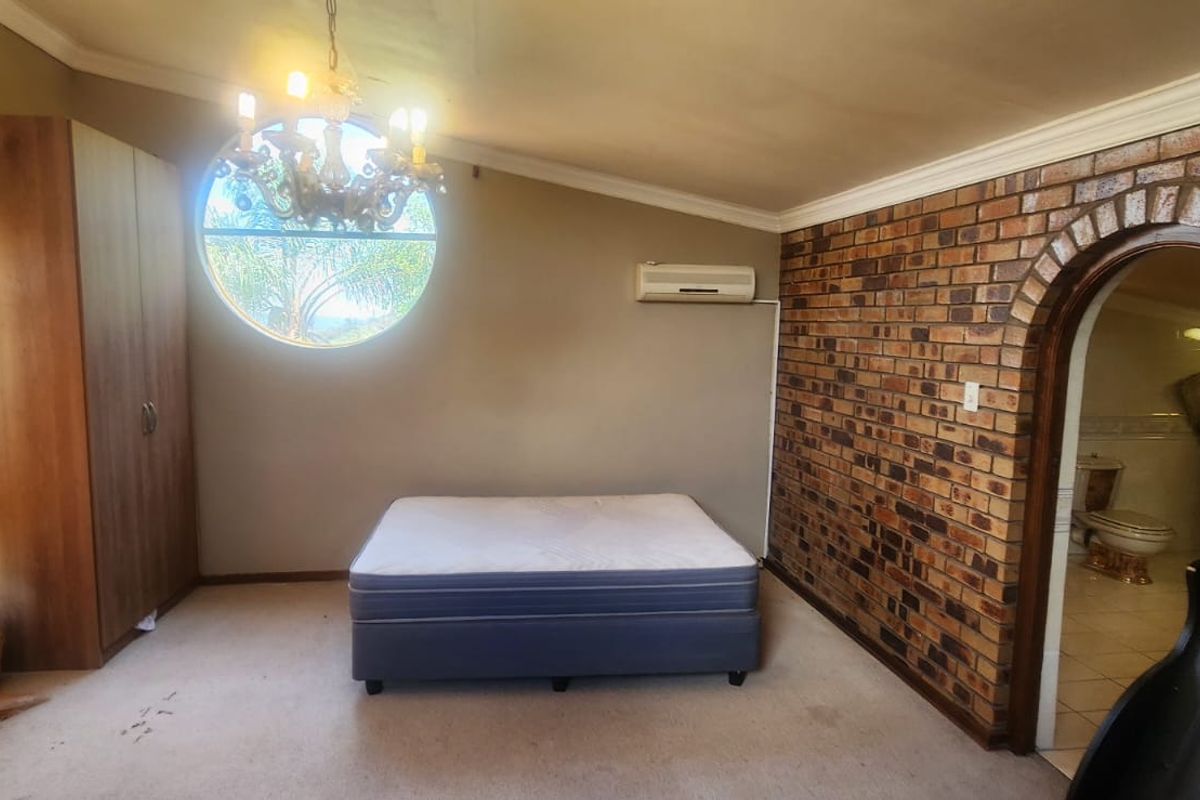 Spacious bedroom featuring an exposed brick feature wall, arched entry to an en-suite, circular window, and wall-mounted air conditioning unit.