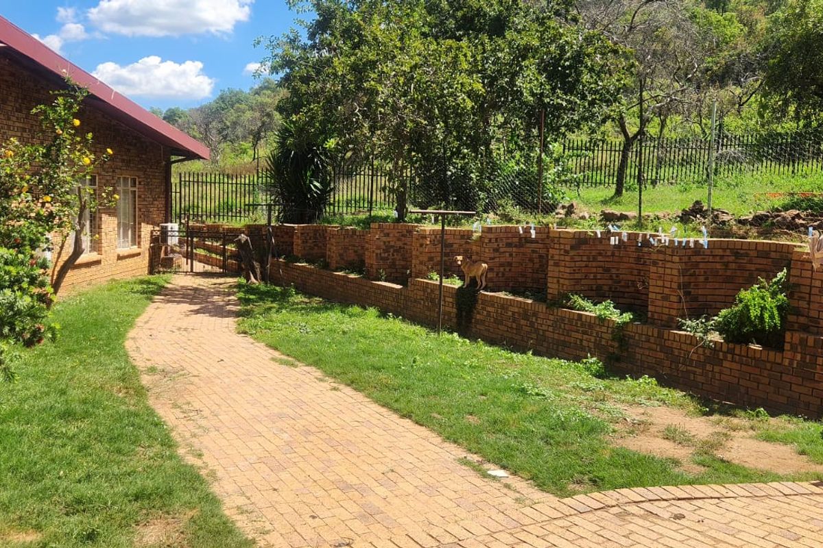 Rear exterior view of the farm property featuring a brick facade, paved walkway, and a brick retaining wall bordering the garden area.