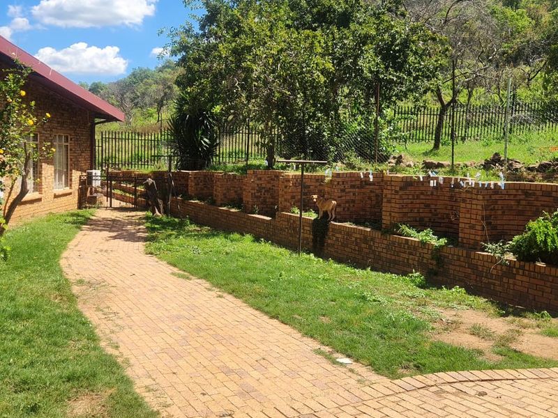 Rear exterior view of the farm property featuring a brick facade, paved walkway, and a brick retaining wall bordering the garden area.