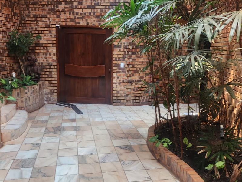 A rustic entrance area featuring face brick walls, tiled flooring, and integrated brick planters leading to a solid wood front door.
