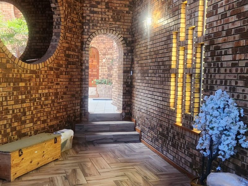 A unique entrance hall featuring exposed brickwork, an arched doorway, a circular window, and stylish herringbone flooring with integrated wall lighting.
