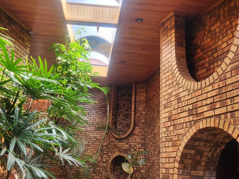 A unique indoor atrium or courtyard space featuring exposed brick walls, arched architectural details, and a timber ceiling with a large central skylight.
