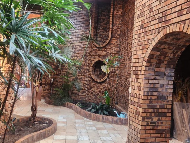 A unique, semi-enclosed courtyard or patio area featuring distinctive exposed brickwork, arched architectural details, and integrated garden beds with tiled flooring.