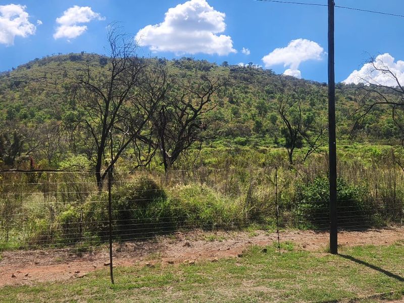 A scenic view of the natural landscape and hillside, featuring a wire boundary fence and utility pole in the foreground.