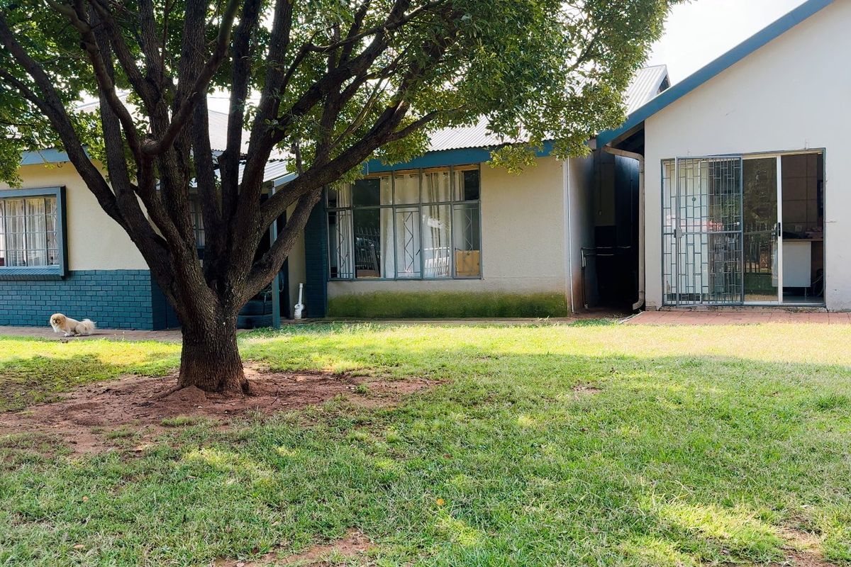 Rear view of the house featuring a paved patio area, security gates, and established garden space with mature trees.
