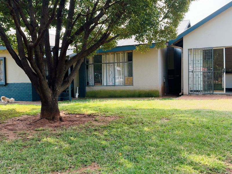 Rear view of the house featuring a paved patio area, security gates, and established garden space with mature trees.
