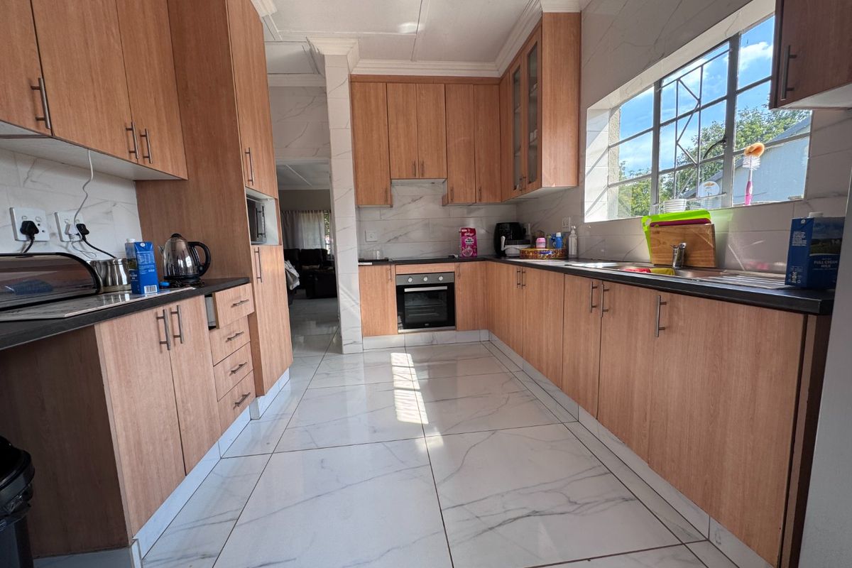 A well-maintained kitchen featuring light wood-finish cabinetry, marble-look tiled flooring, built-in oven and hob, and ample counter space with a large window.