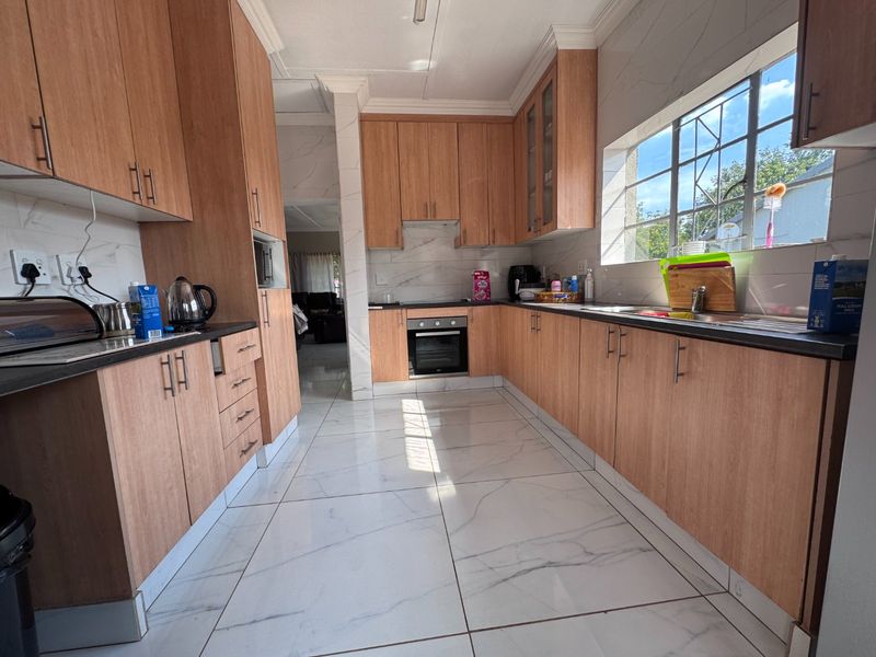 A well-maintained kitchen featuring light wood-finish cabinetry, marble-look tiled flooring, built-in oven and hob, and ample counter space with a large window.