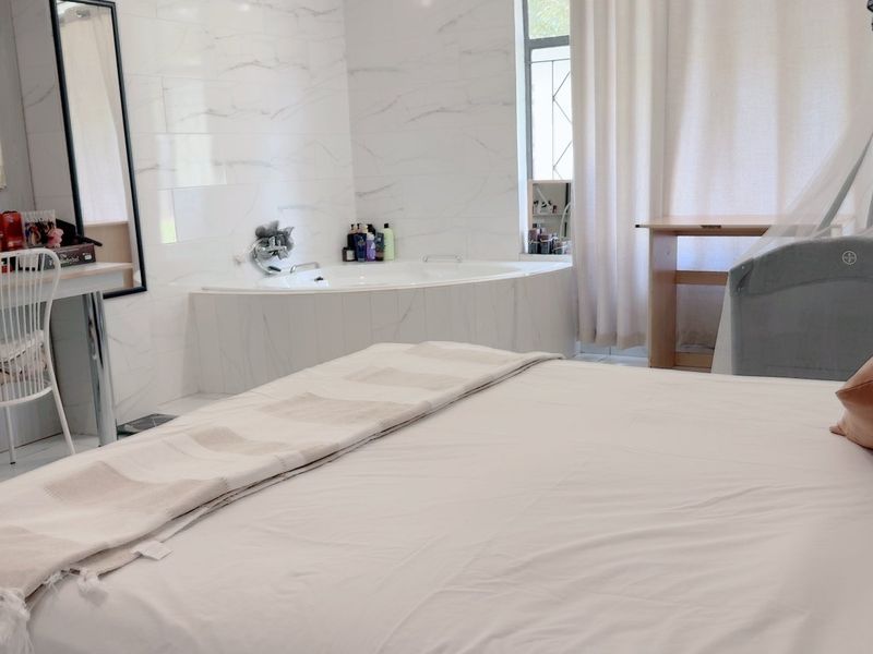 A spacious bedroom featuring an integrated corner bathtub with marble-style wall tiling and modern tiled flooring.