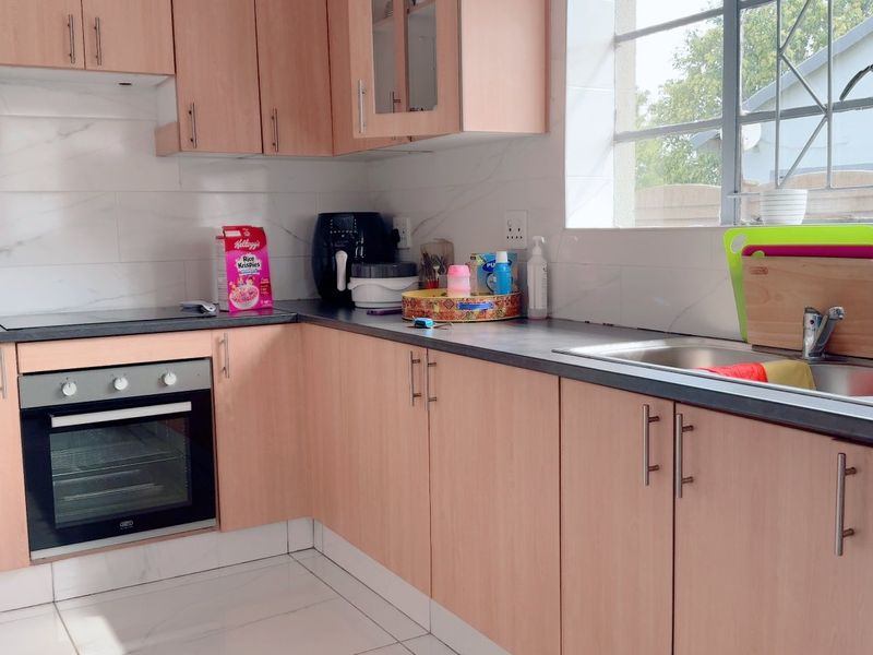 A functional kitchen featuring light wood-tone cabinetry, dark laminate countertops, a built-in oven, electric hob, and tiled finishes throughout.