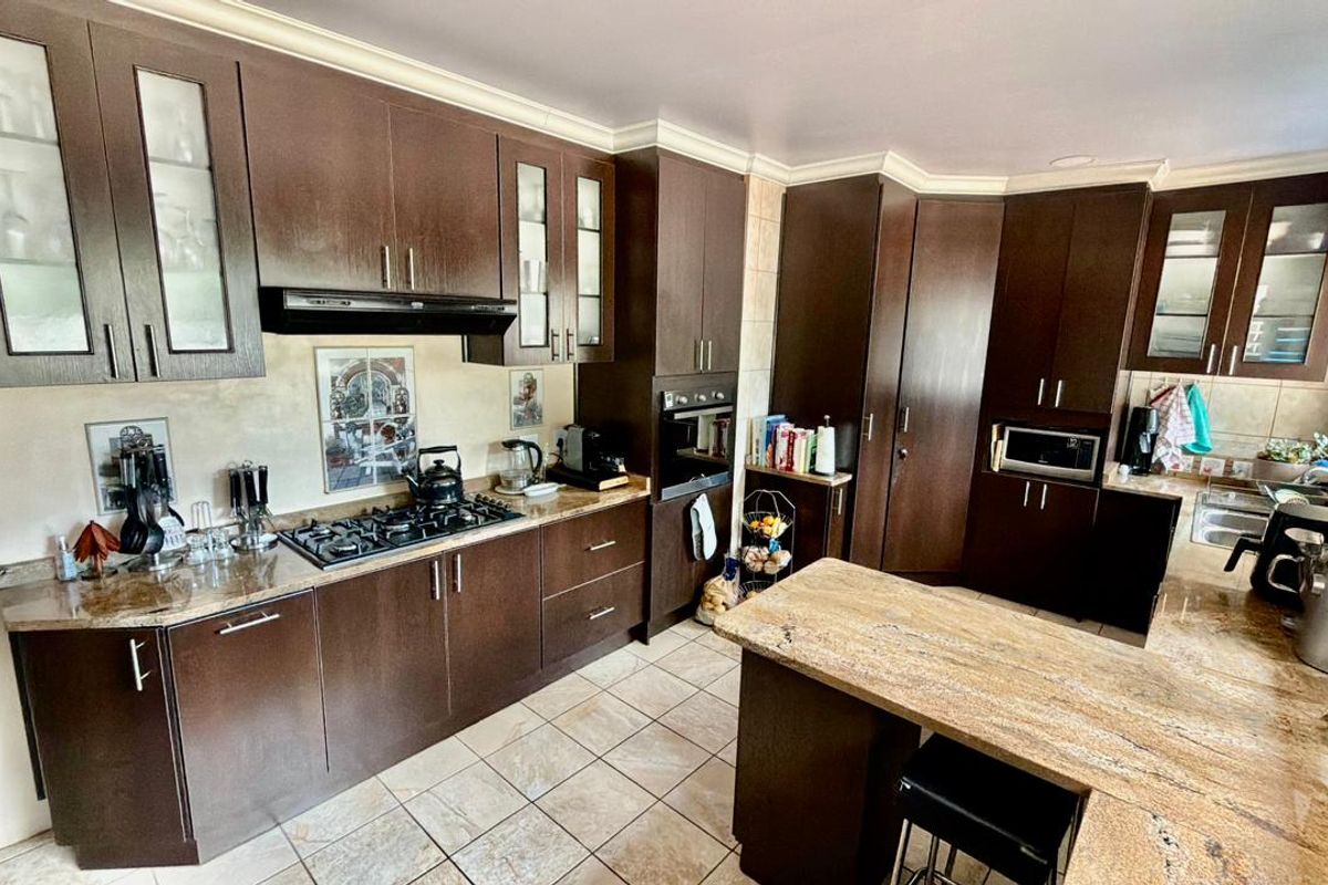 Spacious kitchen featuring dark wood cabinetry, granite countertops, a central island, and built-in appliances including a gas hob and oven.