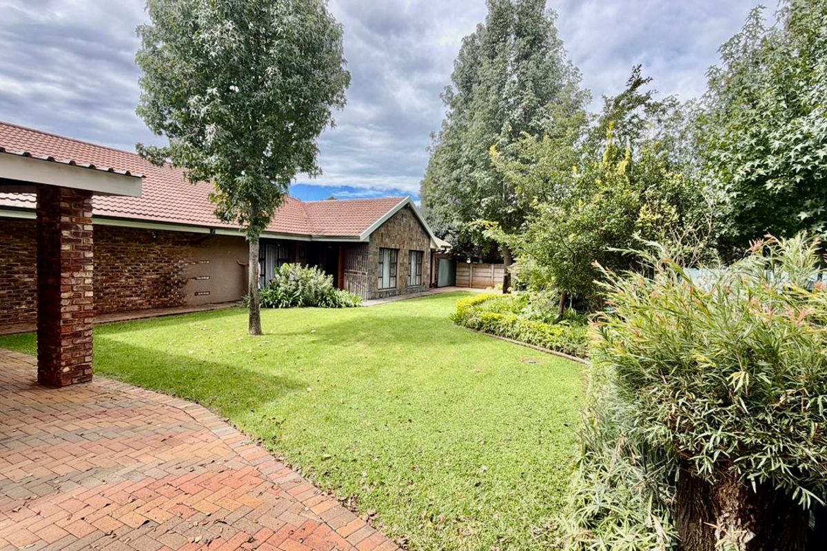 A well-maintained rear garden featuring a brick-paved patio area, established landscaping, and a classic brick and stone-clad house exterior.