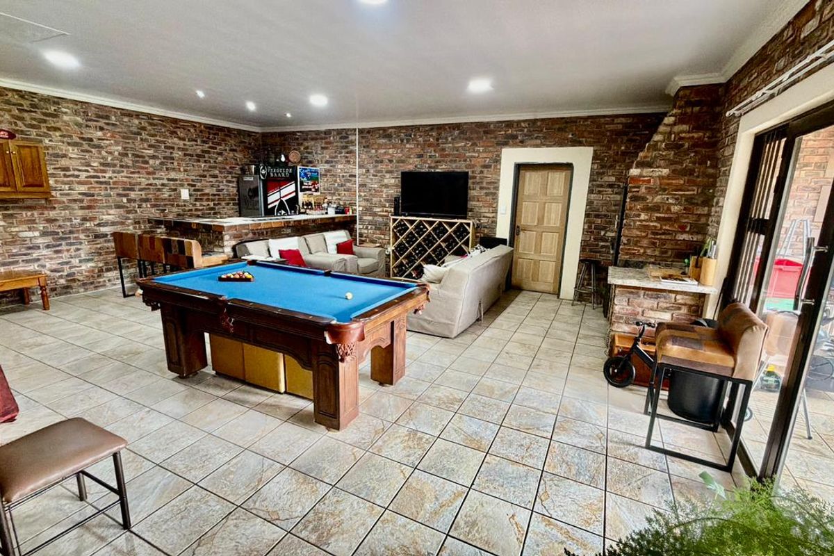 Spacious entertainment room featuring exposed brick walls, tiled flooring, a built-in bar, and direct access to the outdoor area through sliding glass doors.