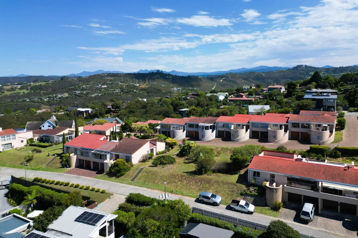 Aerial view of a residential estate featuring multiple homes with red tiled roofs, paved driveways, and landscaped surroundings set against a scenic mountain backdrop.