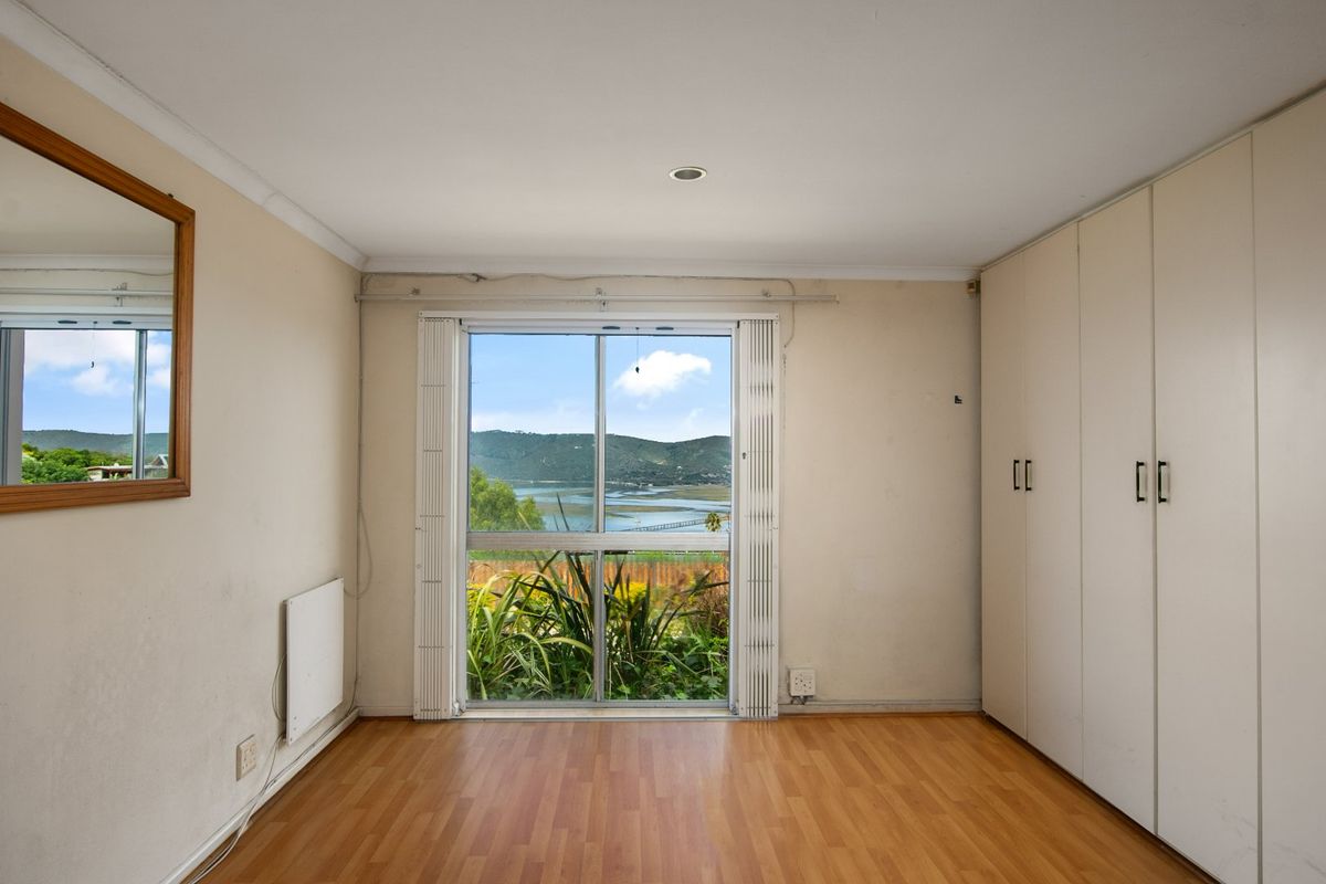 A bedroom featuring built-in wardrobes, laminate flooring, and a large window offering scenic water and landscape views.