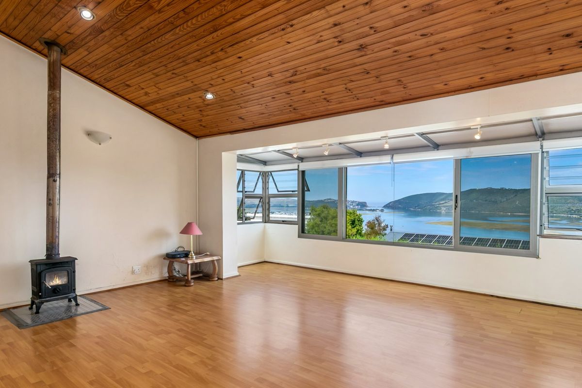Spacious living area featuring a wood-burning fireplace, timber-clad ceiling, and expansive windows offering panoramic water and mountain views.
