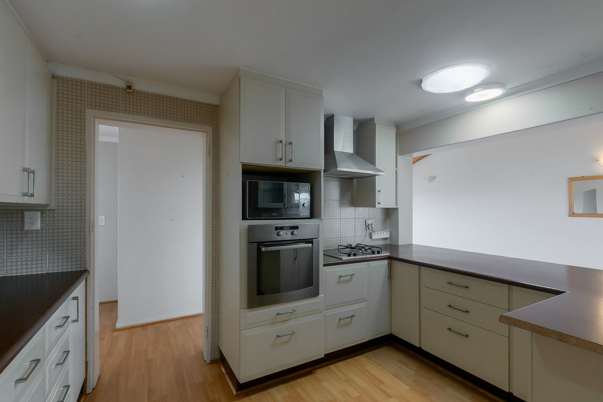 A functional kitchen featuring built-in cabinetry, a stainless steel oven, microwave, gas hob, and extractor fan with laminate countertops and wood-look flooring.