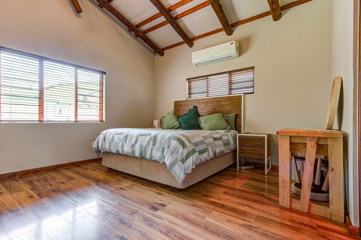 A well-maintained bedroom featuring exposed timber ceiling beams, laminate wood flooring, and a wall-mounted split-system air conditioning unit.
