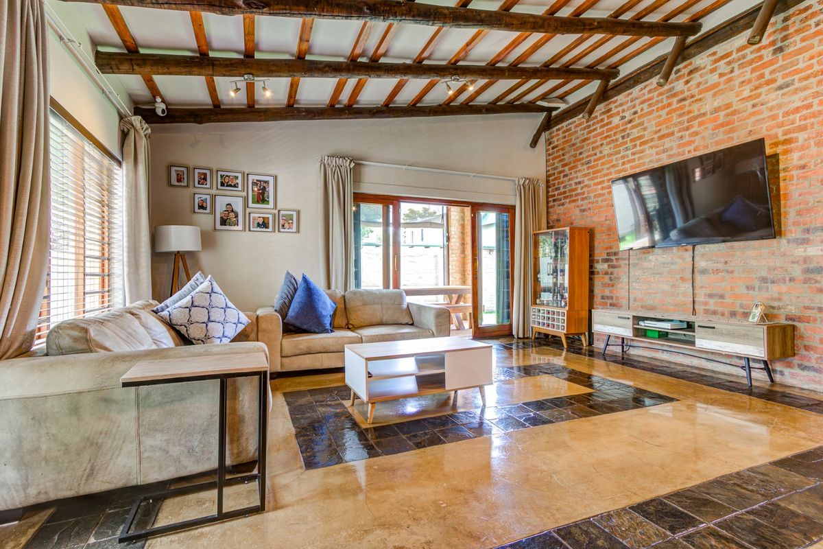 Spacious living room featuring exposed timber ceiling beams, a rustic brick feature wall, and polished concrete flooring with decorative tile inlay.
