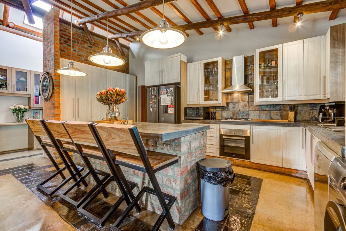 Spacious kitchen featuring exposed brick walls, timber ceiling beams, a central island with stone countertop, and high-quality built-in cabinetry and appliances.