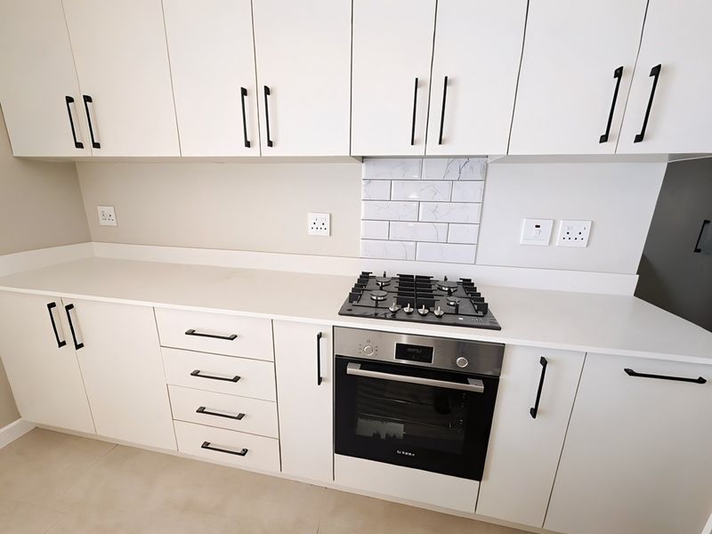 Modern kitchen featuring white cabinetry, stone countertops, a gas hob, built-in oven, and a stylish subway tile splashback.