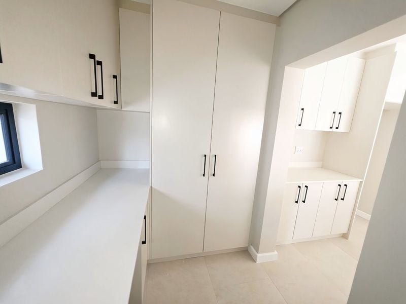 A clean, modern scullery featuring ample built-in cabinetry, stone countertops, and neutral tiled flooring, providing excellent additional storage and prep space.