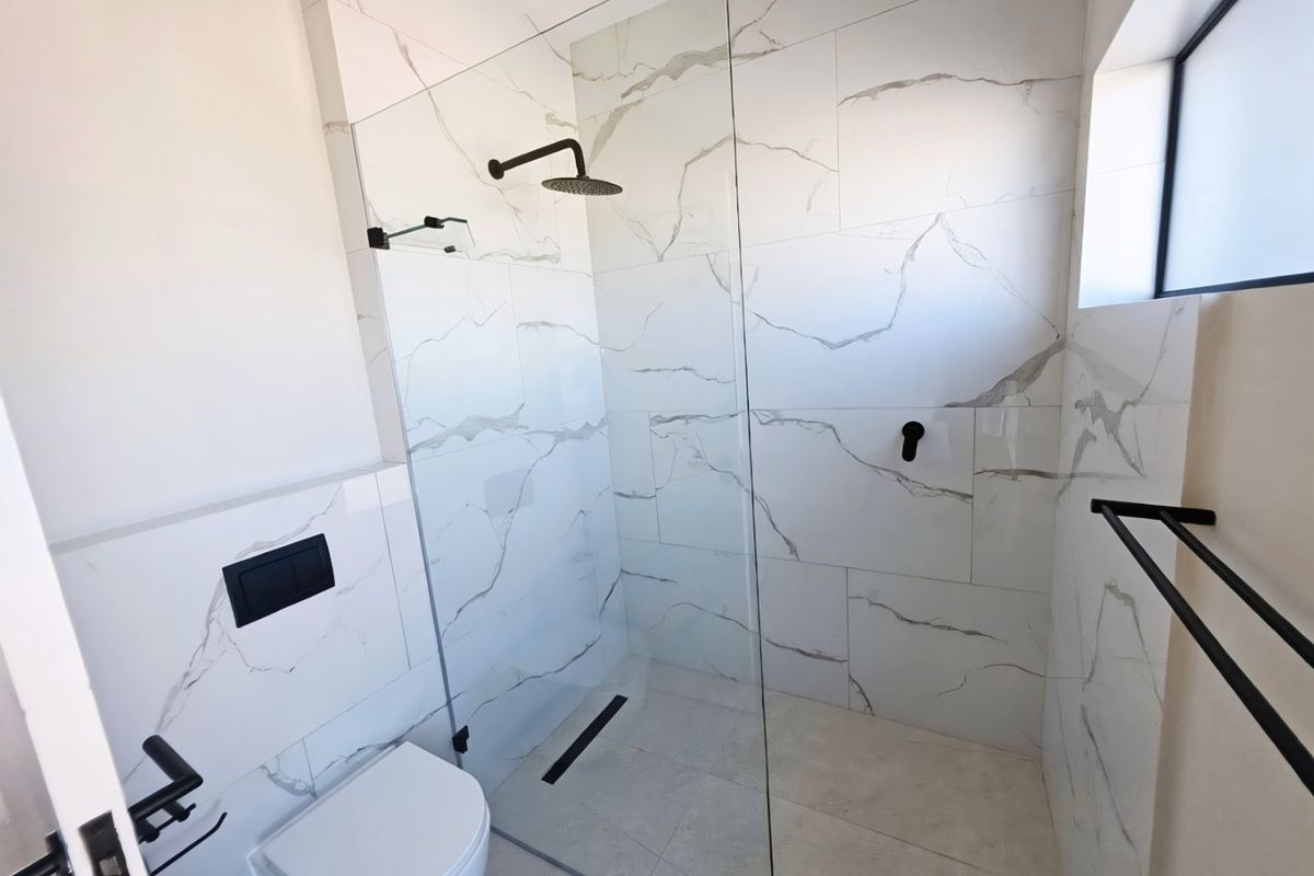 Modern bathroom featuring a walk-in shower with glass screen, rain shower head, wall-mounted toilet with concealed cistern, and elegant marble-look wall tiling.