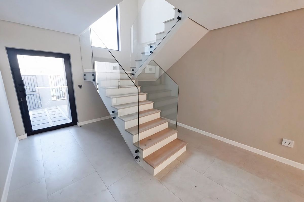 Modern entrance hall featuring a contemporary timber staircase with a sleek glass balustrade and large format floor tiles.