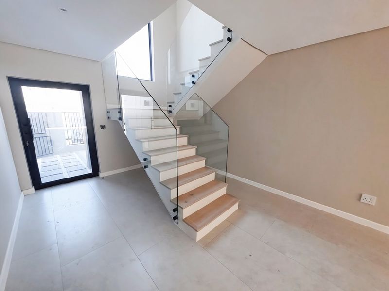 Modern entrance hall featuring a contemporary timber staircase with a sleek glass balustrade and large format floor tiles.