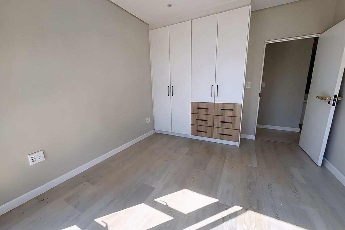 A bright, modern bedroom featuring light timber flooring and contemporary built-in cupboards with a mix of white and wood-grain finishes.