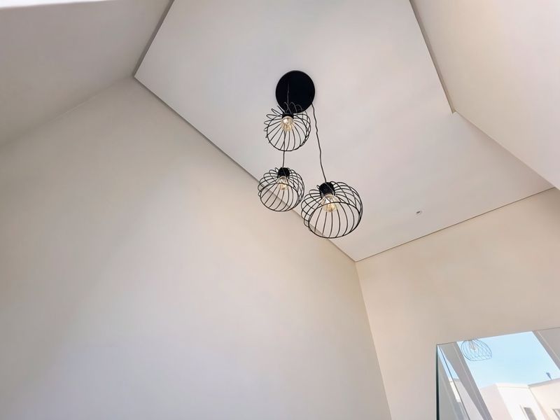 A low-angle view of a modern interior space featuring a recessed ceiling design and a contemporary three-bulb black wire pendant light fixture.