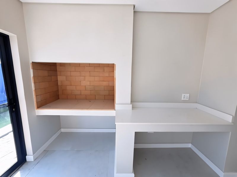 A clean, modern covered patio area featuring a built-in brick braai and a sleek preparation counter with an integrated electrical point.