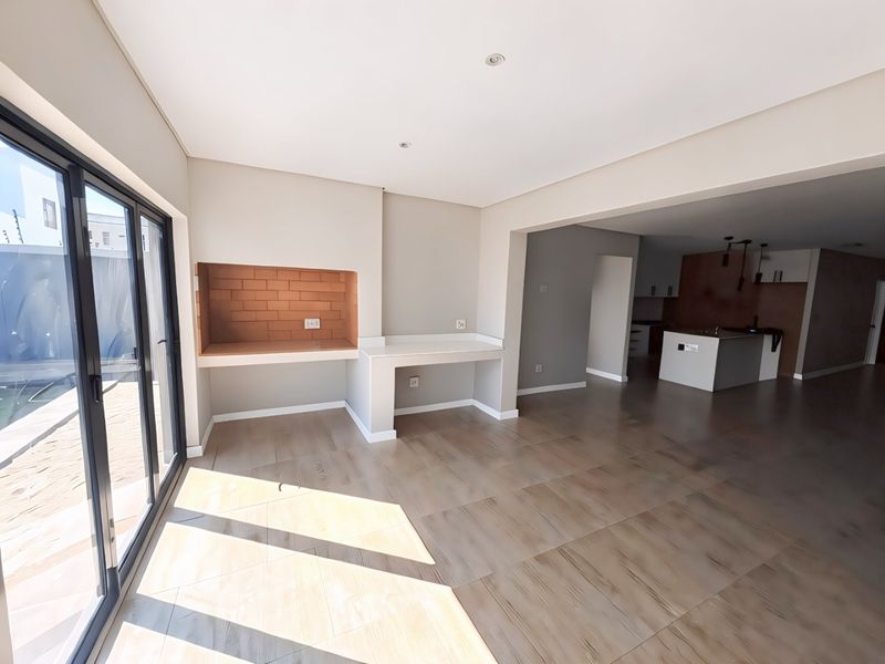Spacious open-plan living area featuring a built-in braai, modern tiled flooring, and seamless flow to the kitchen with a central island.